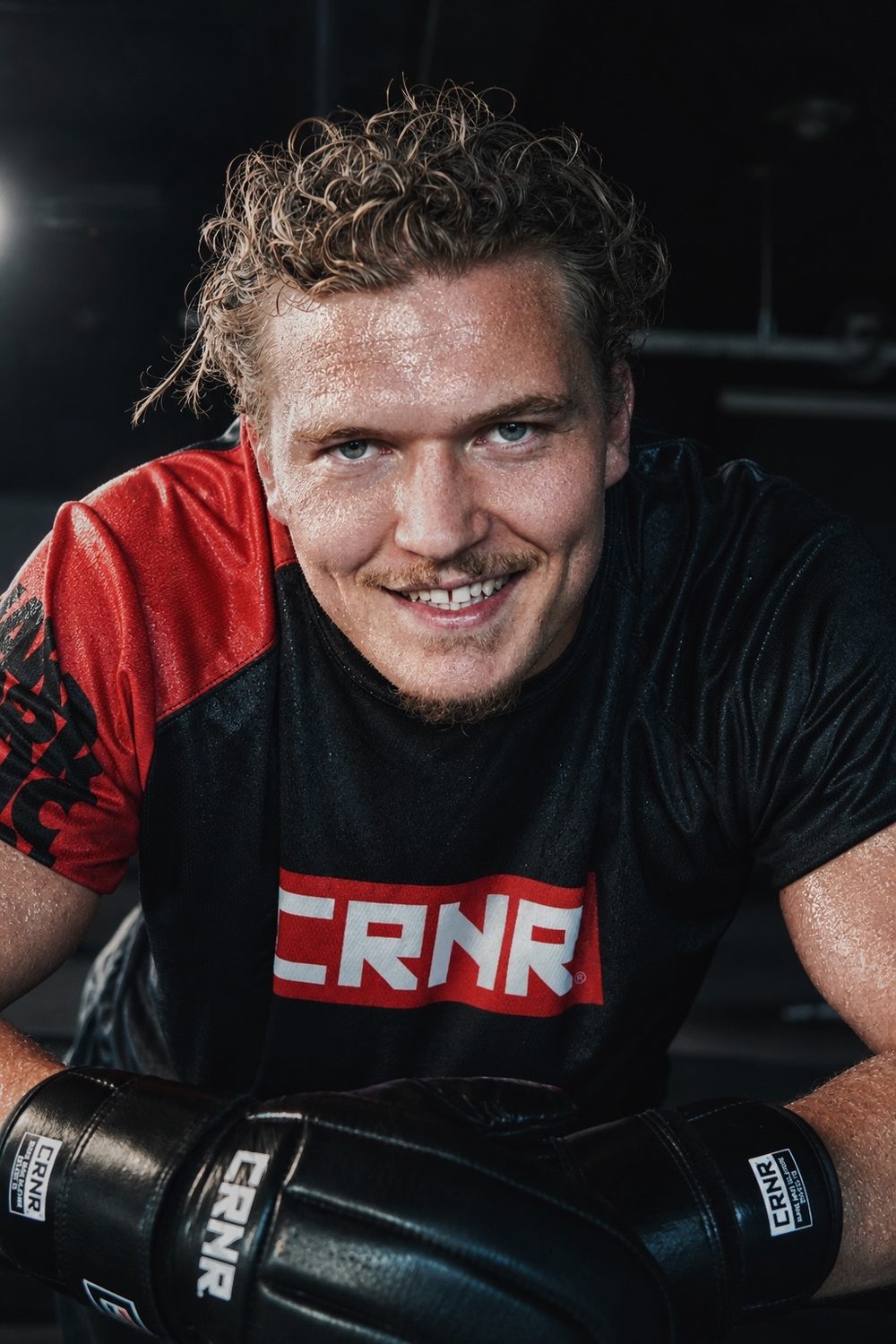 Smilende utøver i trøye fra CRNR, med boksehanskene foran seg